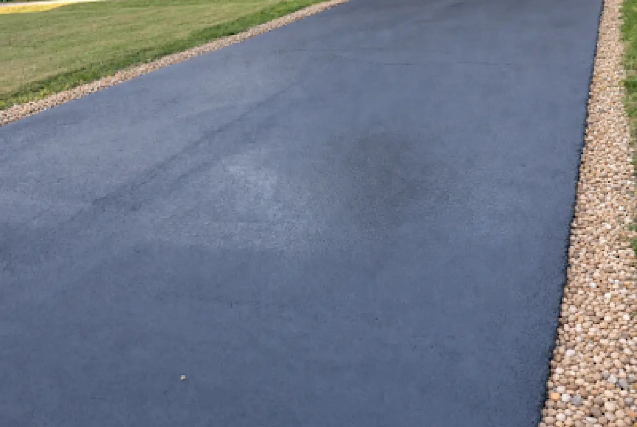 Worker applying asphalt sealcoat to a residential driveway with a squeegee